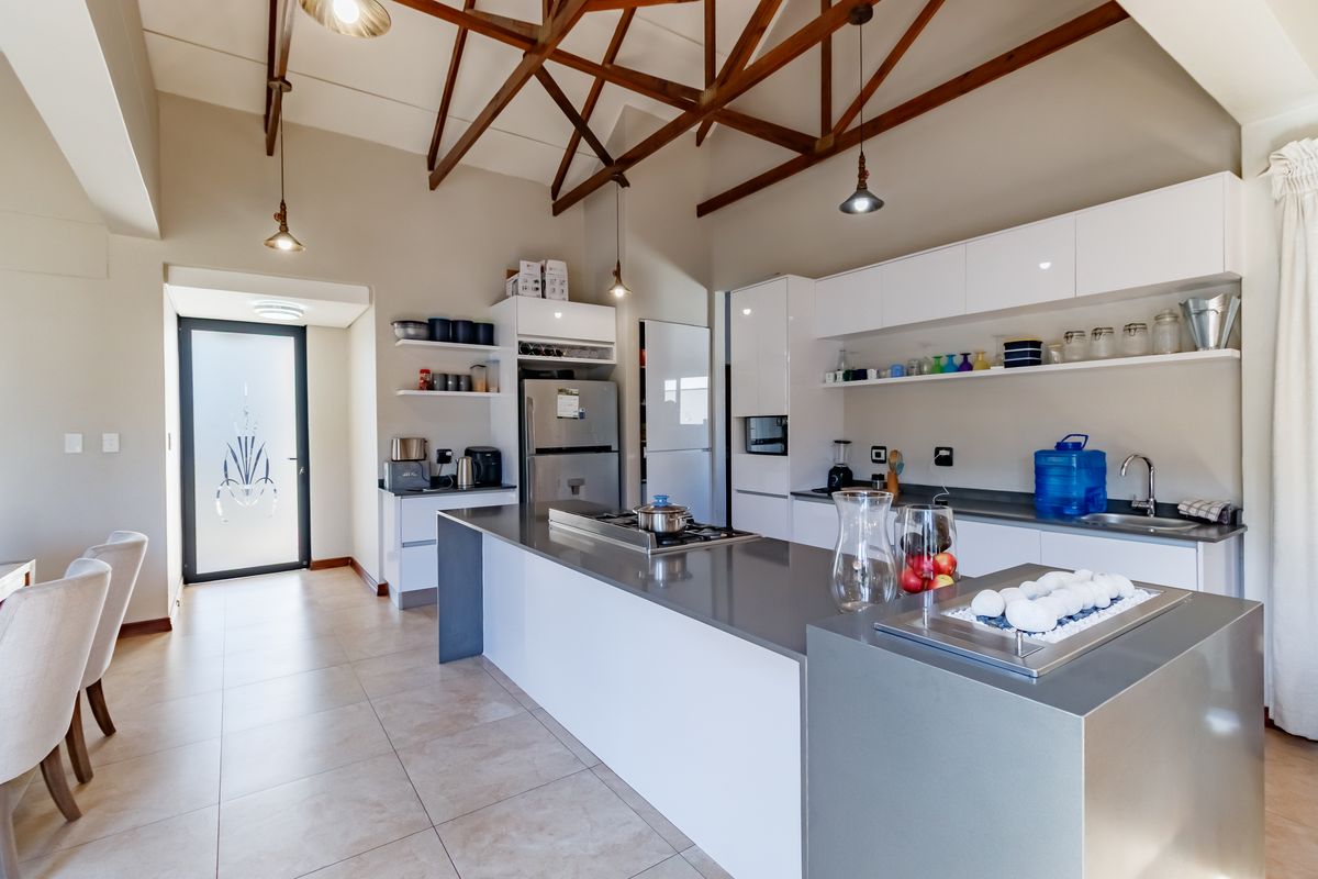 Modern kitchen featuring a large central island with stone countertops, sleek white cabinetry, and striking exposed timber roof trusses.