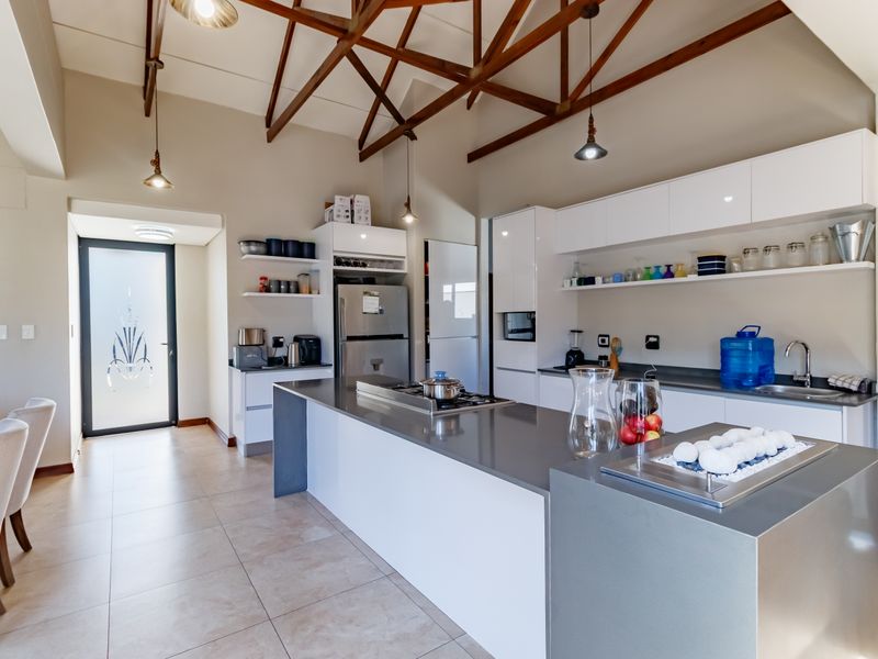 Modern kitchen featuring a large central island with stone countertops, sleek white cabinetry, and striking exposed timber roof trusses.