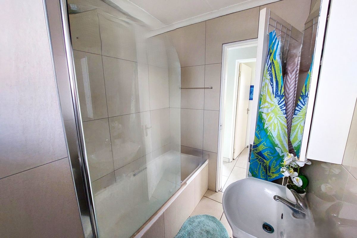 A functional bathroom featuring a built-in bathtub with a glass shower screen, tiled walls, and a wall-mounted basin.
