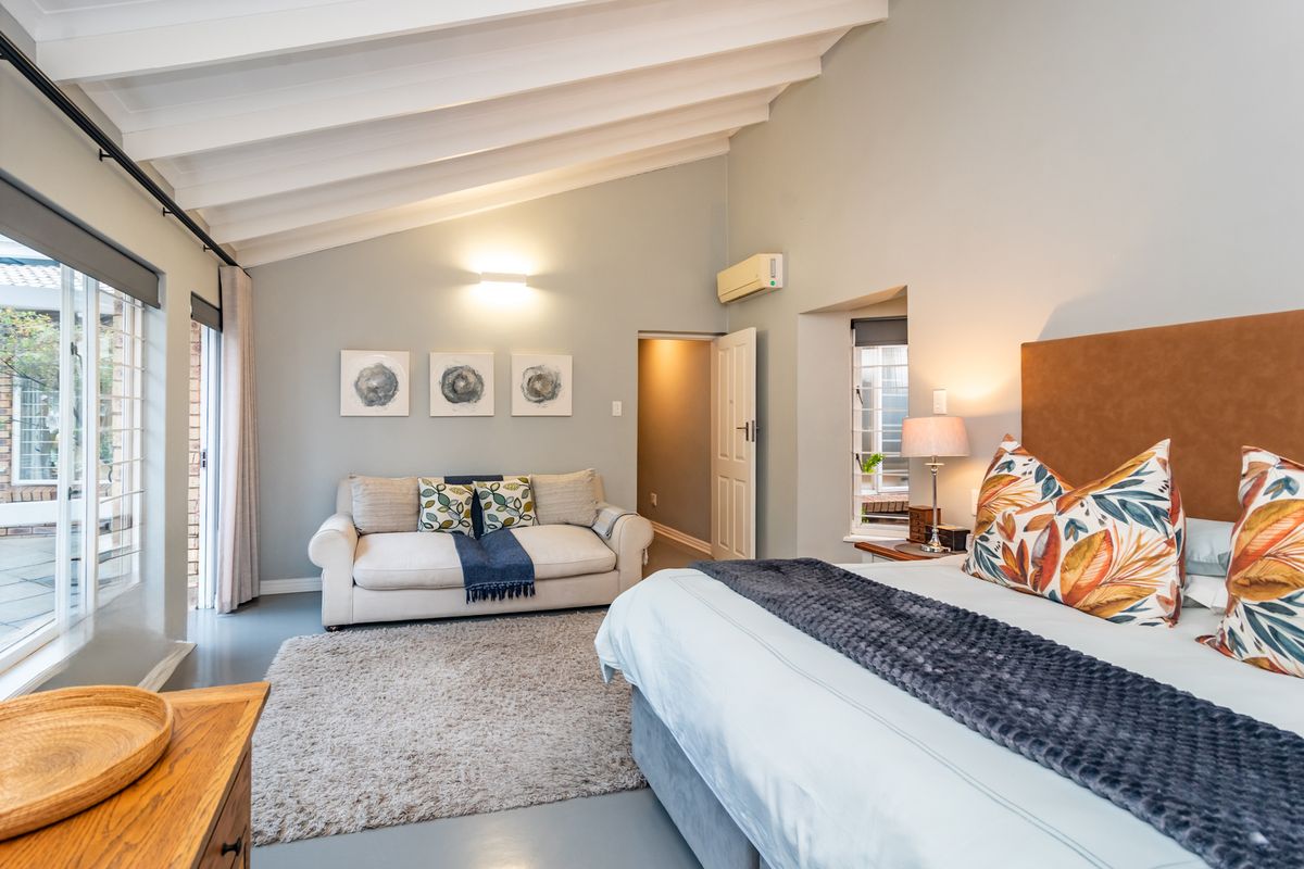 Spacious bedroom featuring a vaulted ceiling with exposed beams, neutral wall tones, and direct access to an outdoor patio area through sliding glass doors.