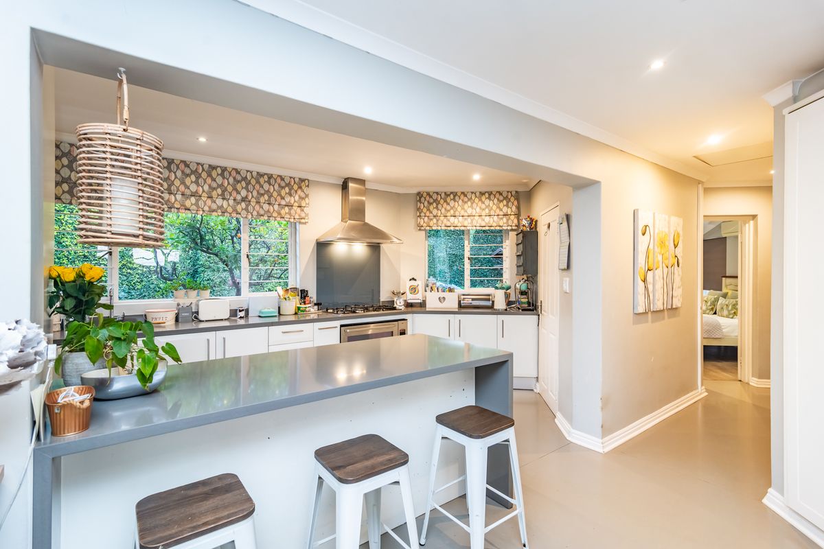 Modern kitchen featuring a central island with stone countertops, stainless steel extractor fan, built-in oven, and ample cabinetry, seamlessly flowing into the living area.