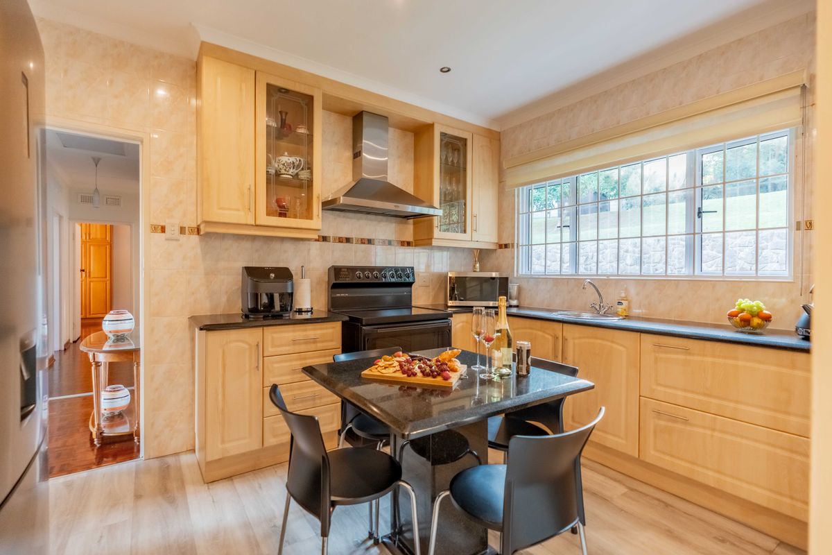 A well-maintained kitchen featuring light wood cabinetry, black granite countertops, a stainless steel extractor fan, and a tiled splashback with a view to the garden.