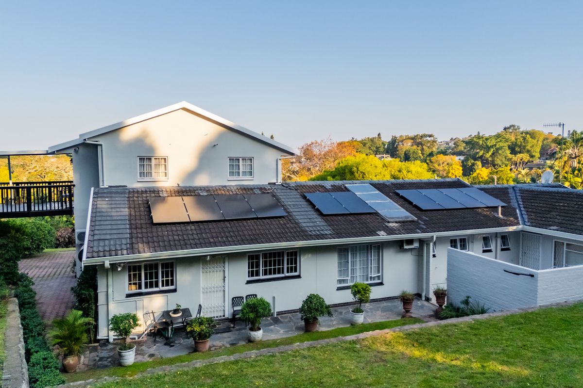 Rear view of the property featuring a tiled roof with installed solar panels, a stone patio area, and a well-maintained garden.