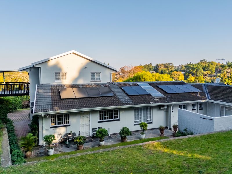 Rear view of the property featuring a tiled roof with installed solar panels, a stone patio area, and a well-maintained garden.