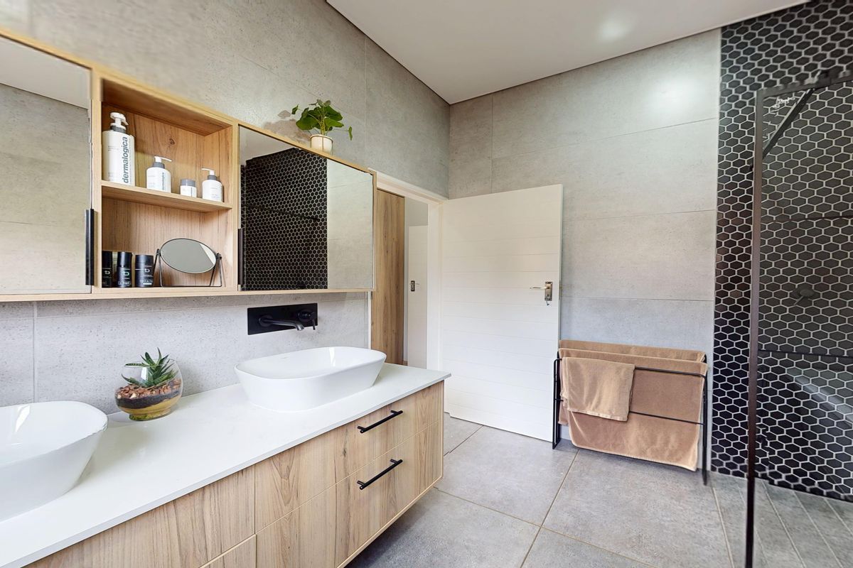 Modern bathroom featuring a double vanity with vessel sinks, wall-mounted faucets, wood-tone cabinetry, and a walk-in shower with stylish black hexagon mosaic tiles.