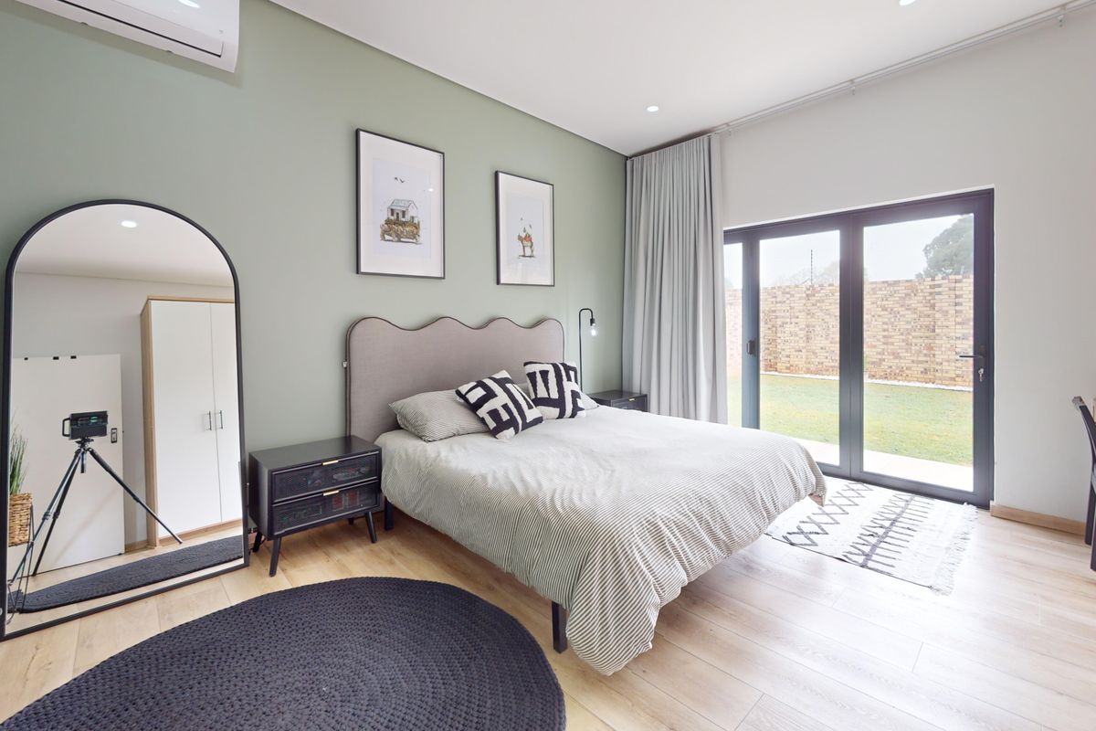 A well-maintained bedroom featuring light laminate flooring, a split-system air conditioner, and large sliding glass doors providing direct access to the rear garden.