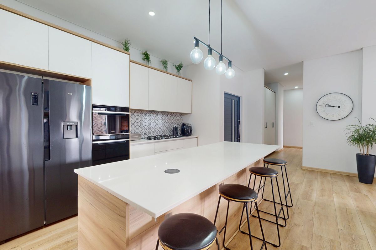 Modern kitchen featuring a large island with stone countertop, integrated cabinetry, built-in oven, gas hob, and stylish patterned tile splashback.