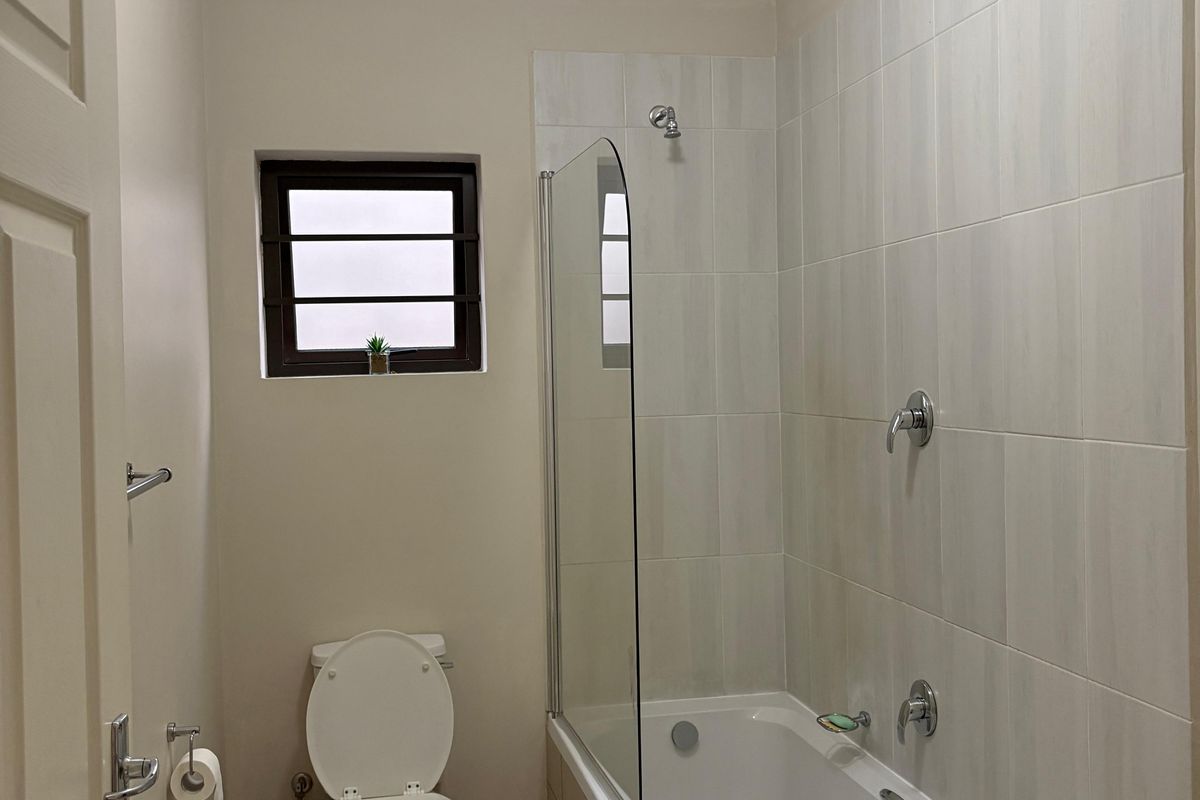 A clean and functional bathroom featuring a bathtub with a glass shower screen, tiled walls, and a standard toilet.