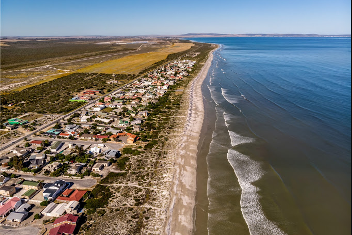 An aerial view of a coastal residential area situated along a sandy beach, showcasing the proximity to the ocean and surrounding landscape.