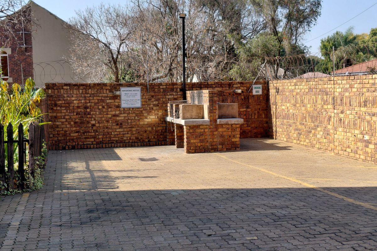 Outdoor communal area featuring a built-in brick braai, paved flooring, and secure brick boundary walls with razor wire fencing.