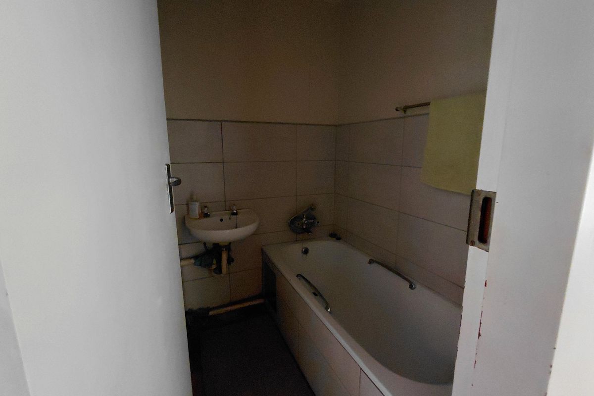 A compact bathroom featuring a standard bathtub, wall-mounted basin, and tiled walls, requiring cosmetic updates to improve its overall condition.
