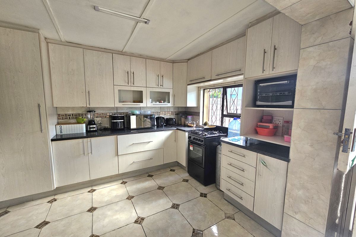 A functional kitchen featuring light-toned laminate cabinetry, granite countertops, a tiled backsplash, and a freestanding stove with ample storage space.