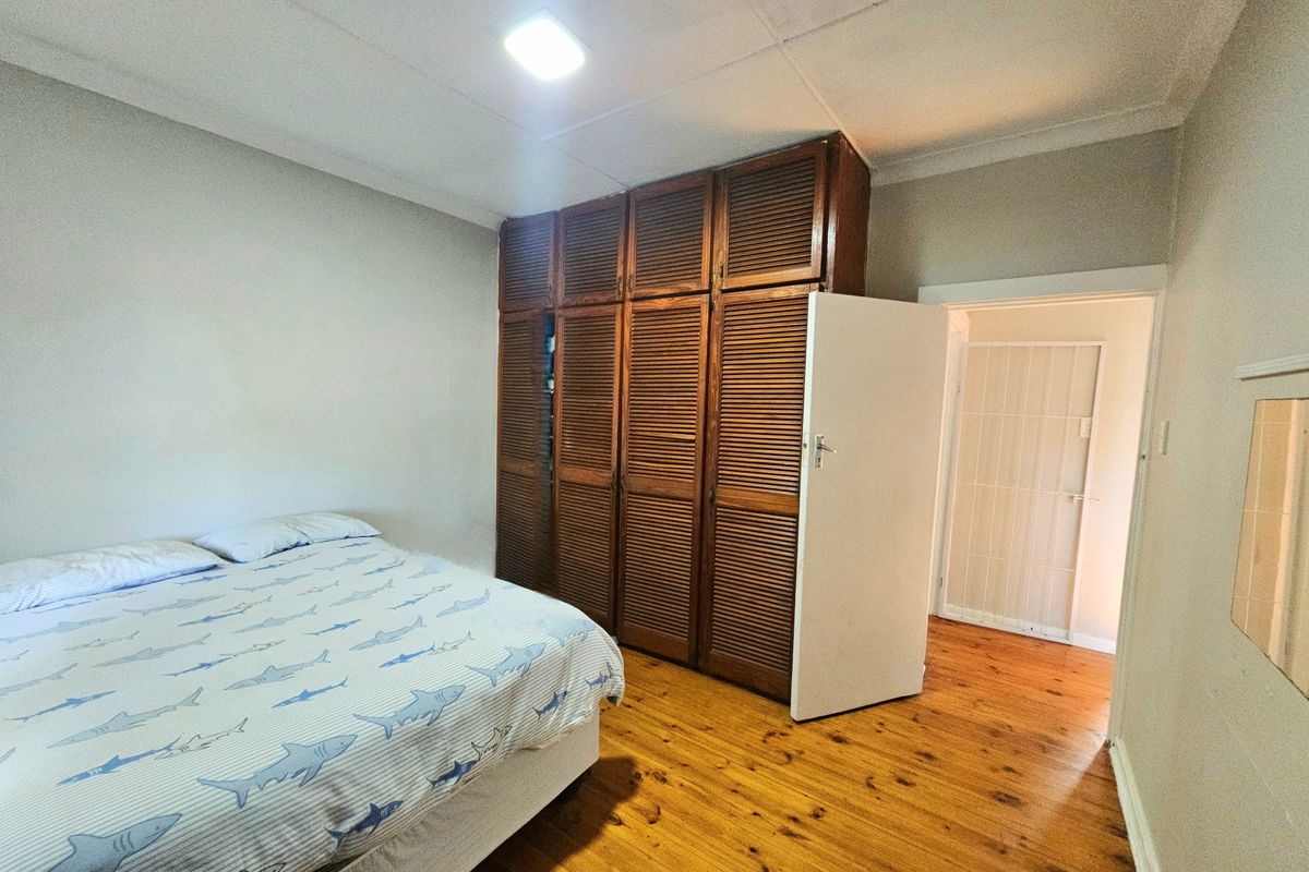 A bedroom featuring timber flooring and a large built-in wooden wardrobe with louvered doors.
