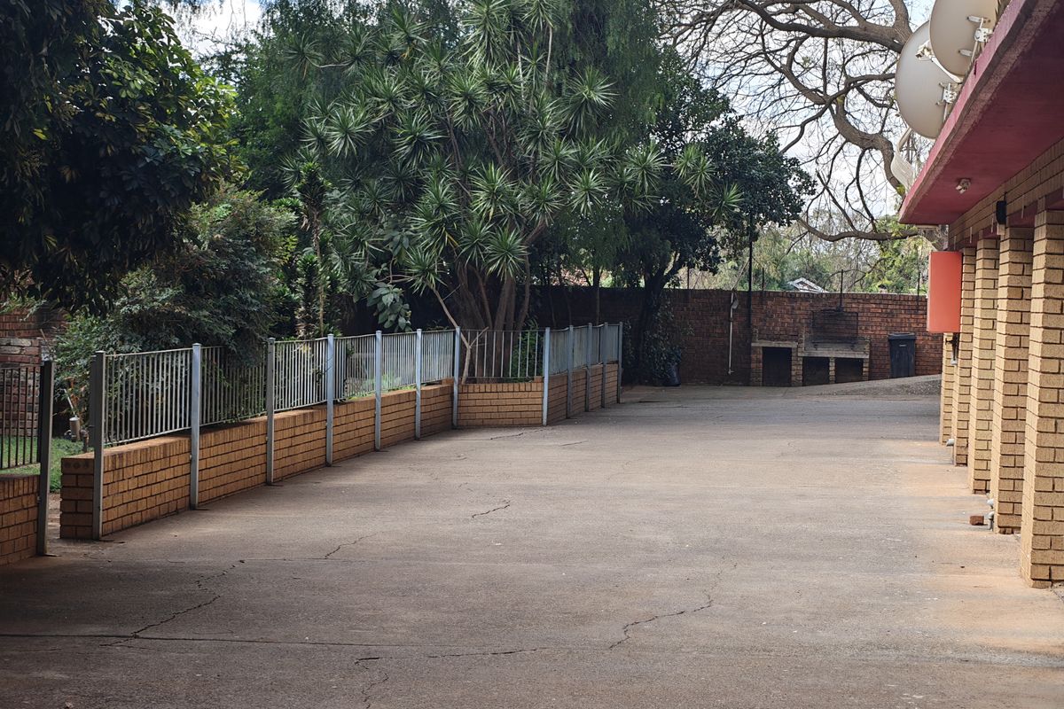 Rear exterior area featuring concrete paving, a built-in brick braai, and perimeter brick walling with metal fencing.