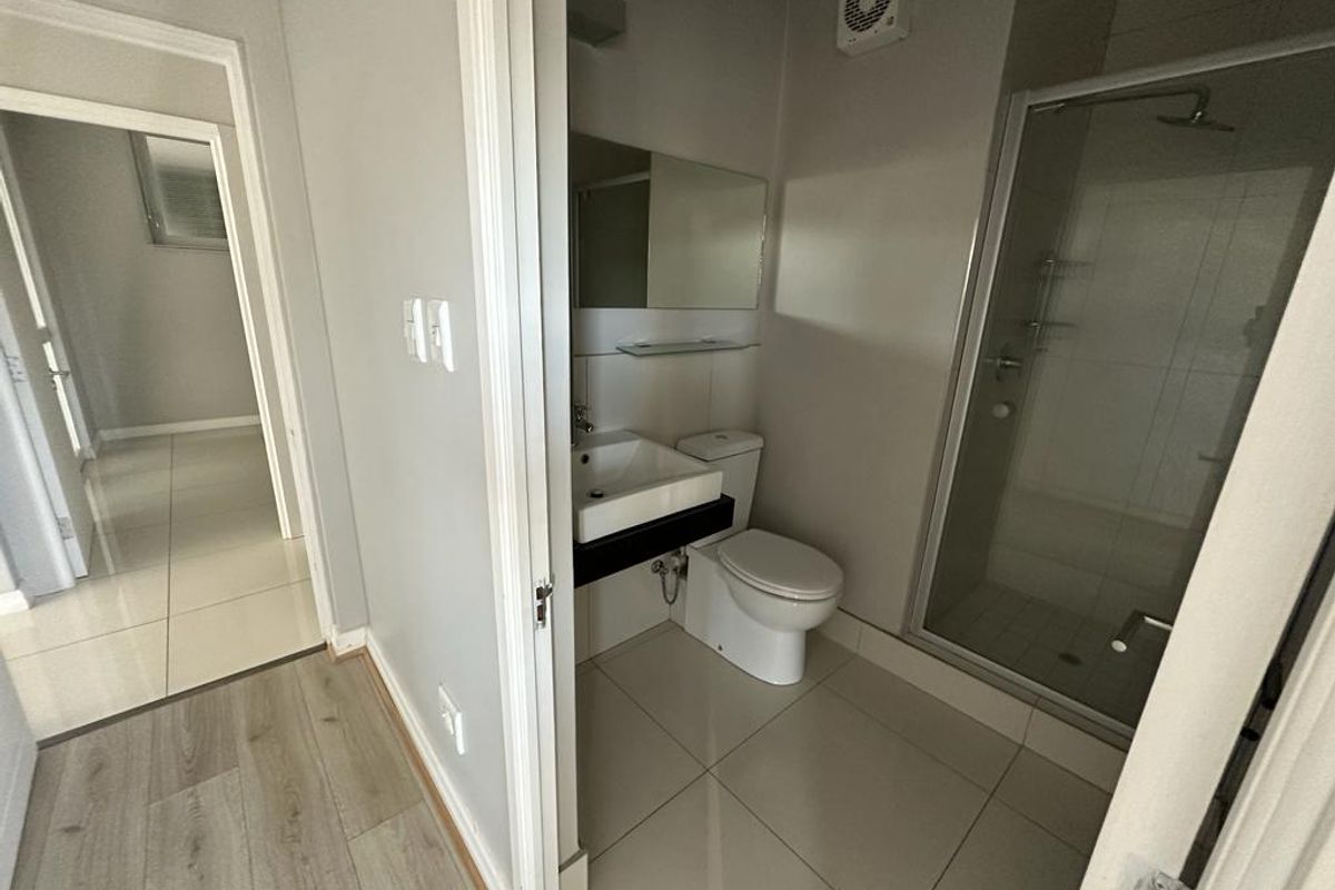 A clean, modern bathroom featuring a glass shower enclosure, wall-mounted basin, and toilet, with neutral tiled flooring and walls.