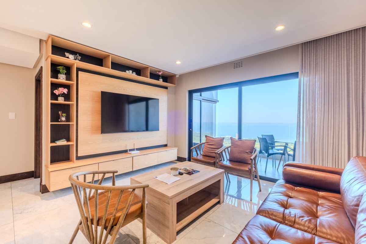 Modern living room featuring custom built-in cabinetry, sleek tiled flooring, and large sliding glass doors opening to a balcony with ocean views.