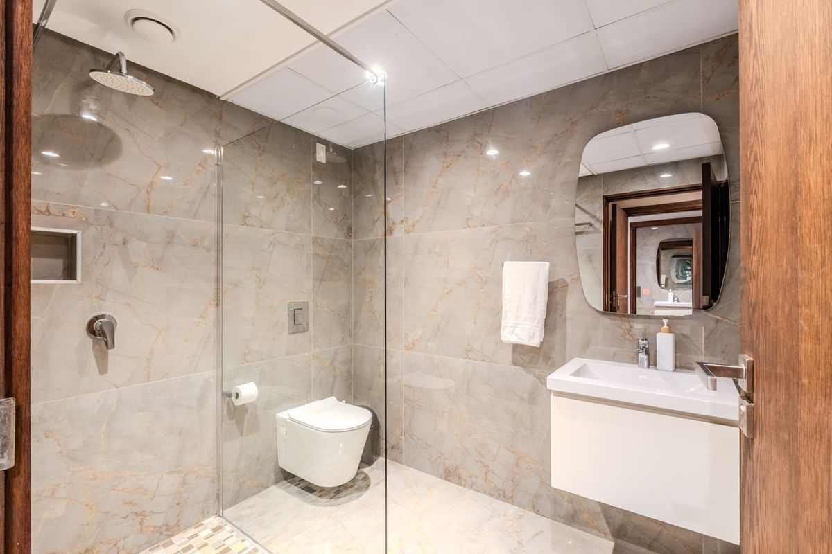 Modern bathroom featuring large-format marble-look wall tiles, a wall-mounted vanity, a glass-enclosed walk-in shower with a rain shower head, and a wall-hung toilet.