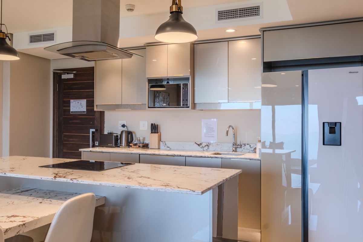 Modern kitchen featuring high-gloss cabinetry, marble-look stone countertops, integrated appliances, and a central island with a built-in induction hob.