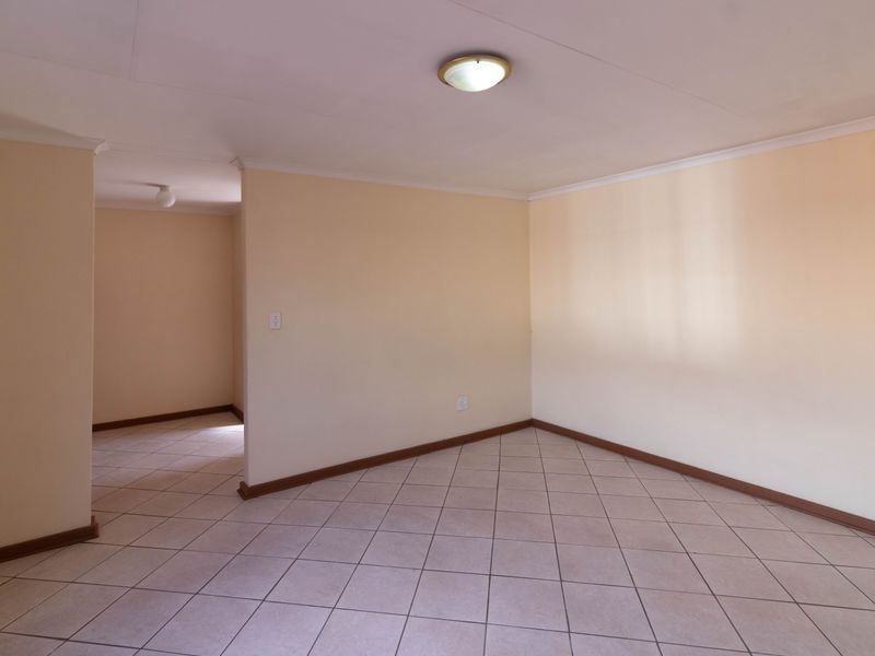 A vacant living area featuring neutral wall paint, tiled flooring, and a simple ceiling-mounted light fixture, offering a clean and versatile space.