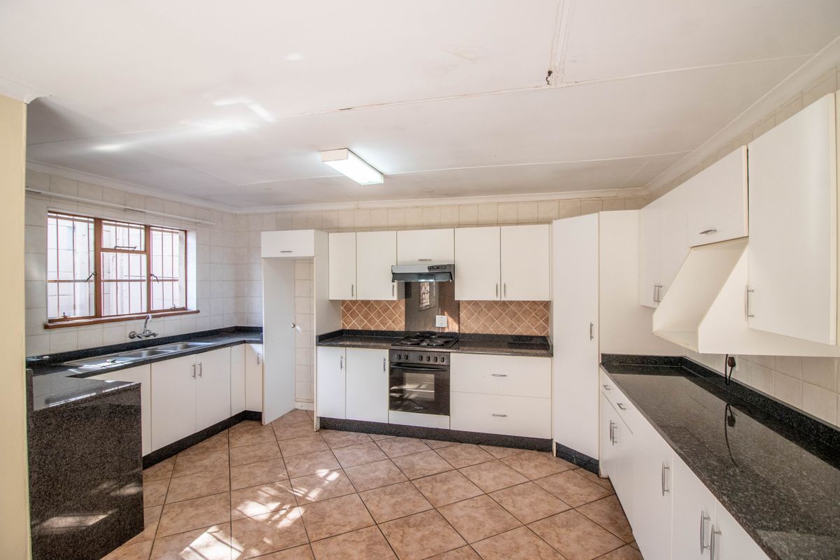 A functional kitchen featuring white cabinetry, dark granite countertops, a built-in oven, hob, extractor fan, and tiled flooring.
