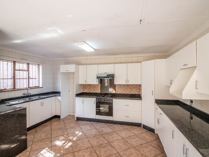 A functional kitchen featuring white cabinetry, dark granite countertops, a built-in oven, hob, extractor fan, and tiled flooring.