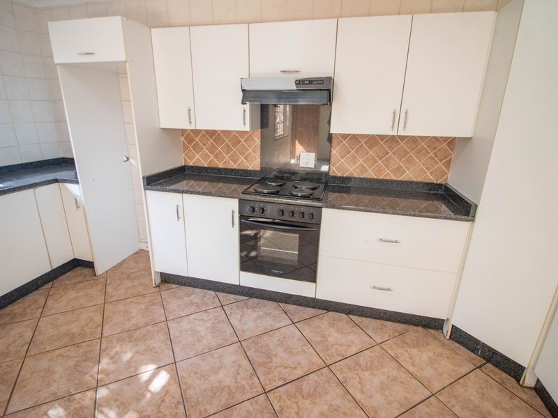 A functional kitchen featuring white cabinetry, dark granite countertops, a built-in oven with hob, and tiled flooring.