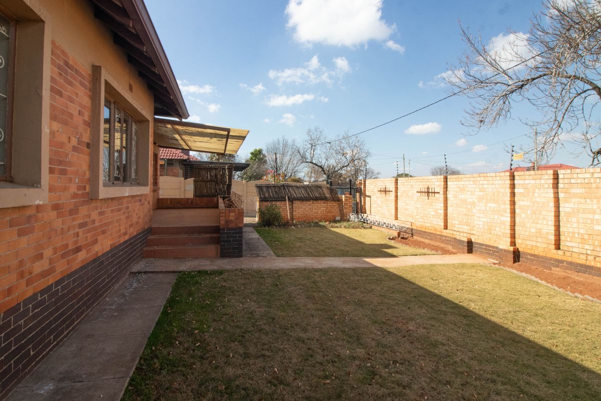 A rear garden featuring a brick-walled perimeter, a paved walkway, and a covered patio area attached to the main house structure.