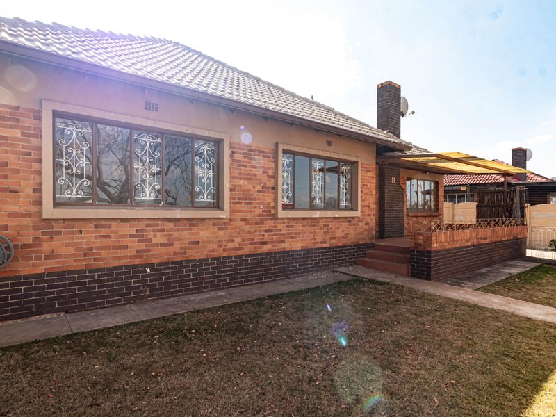A front exterior view of a single-story brick house featuring a tiled roof, security bars on windows, and a small front patio area.