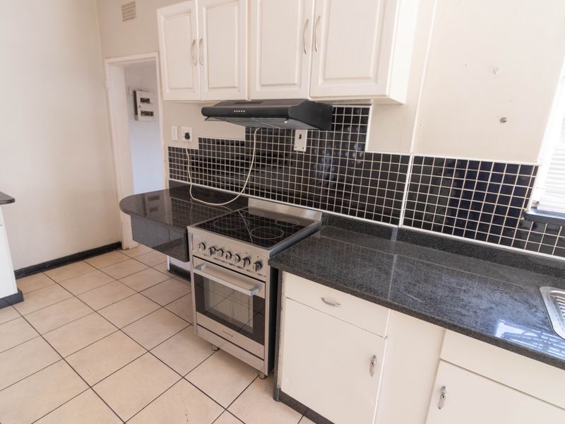 Functional kitchen featuring dark granite countertops, white cabinetry, a built-in stove with extractor fan, and tiled flooring.
