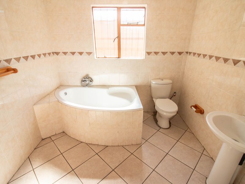 A functional bathroom featuring a corner bathtub, pedestal basin, and toilet with neutral wall and floor tiling.