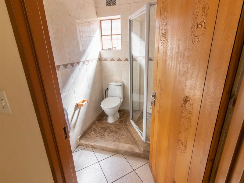A compact bathroom featuring a raised shower enclosure, a standard toilet, and tiled walls with a small window for natural light.