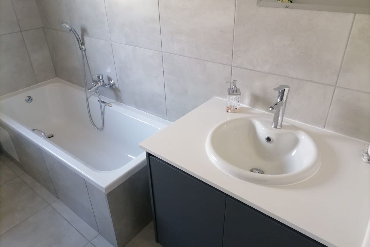 Modern bathroom featuring a built-in bathtub with handheld shower attachment and a contemporary vanity unit with a white basin.