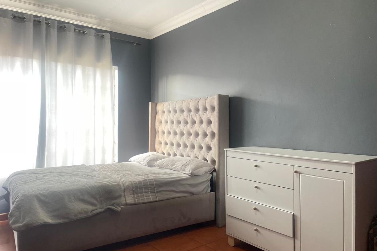 A bedroom featuring dark grey accent walls, crown molding, and tiled flooring with natural light entering through a large window.