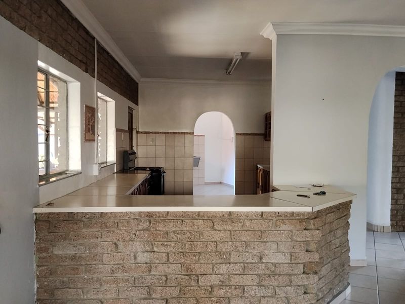 A dated kitchen featuring an exposed brick breakfast bar, tiled backsplash, and archway transitions, offering a blank canvas for modern renovation.