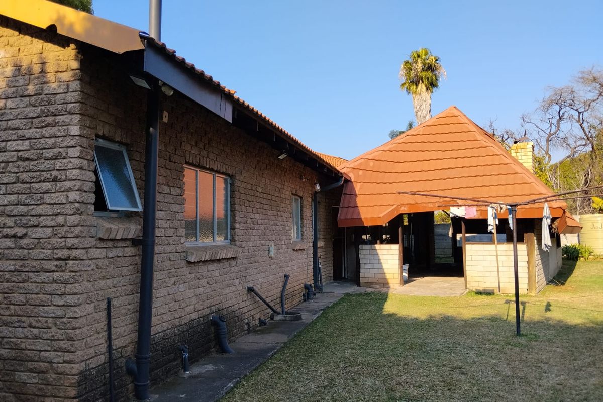 Rear view of the house showing brick exterior, tiled roof, and a covered patio area adjacent to the garden.