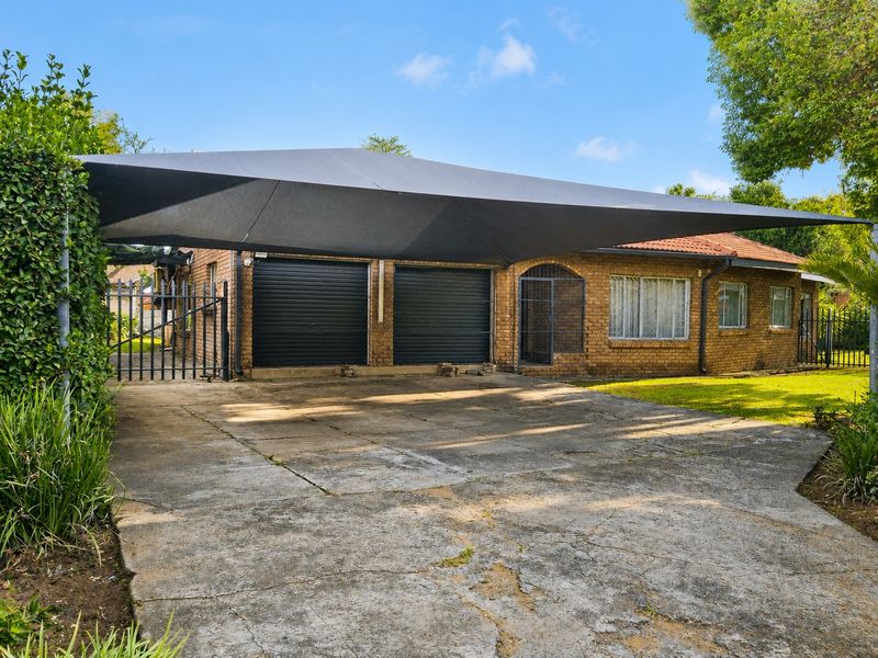 Front exterior view featuring a large shade sail covering a double garage with roller shutter doors and a concrete driveway.