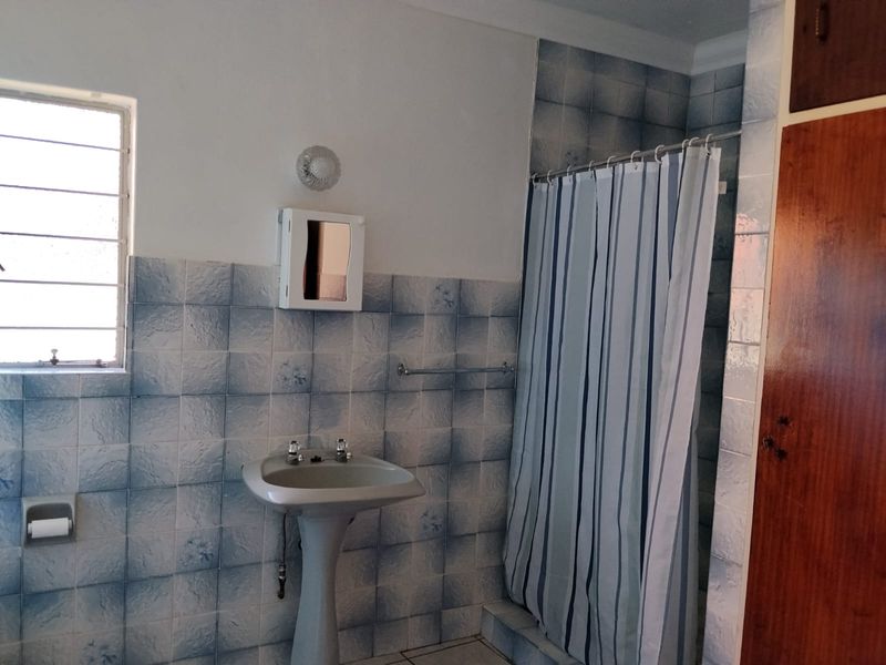 A functional bathroom featuring a pedestal basin, shower area with curtain, and built-in wooden storage cabinetry with dated wall tiling.