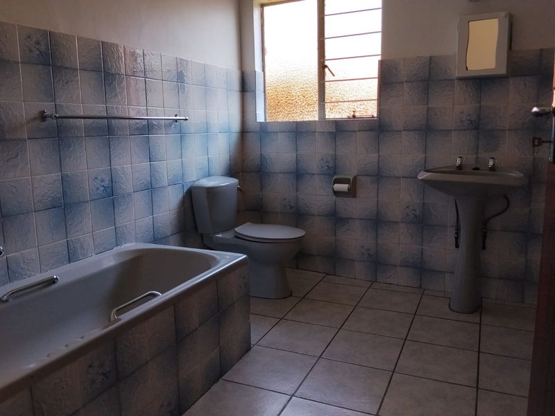 A functional bathroom featuring a bathtub, pedestal basin, and toilet, finished with dated blue-patterned wall tiles and neutral floor tiles.
