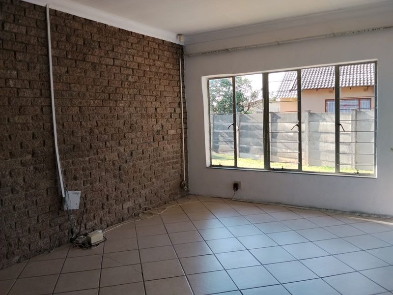 An empty living room featuring a prominent exposed brick wall, tiled flooring, and large windows with security bars.
