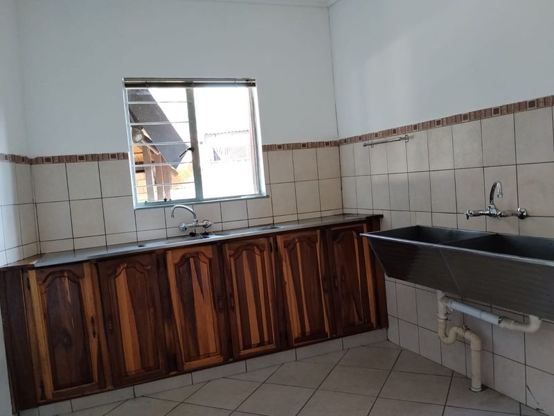 A functional scullery or laundry area featuring built-in wooden cabinetry, a stainless steel sink, a double basin, and tiled splashbacks.