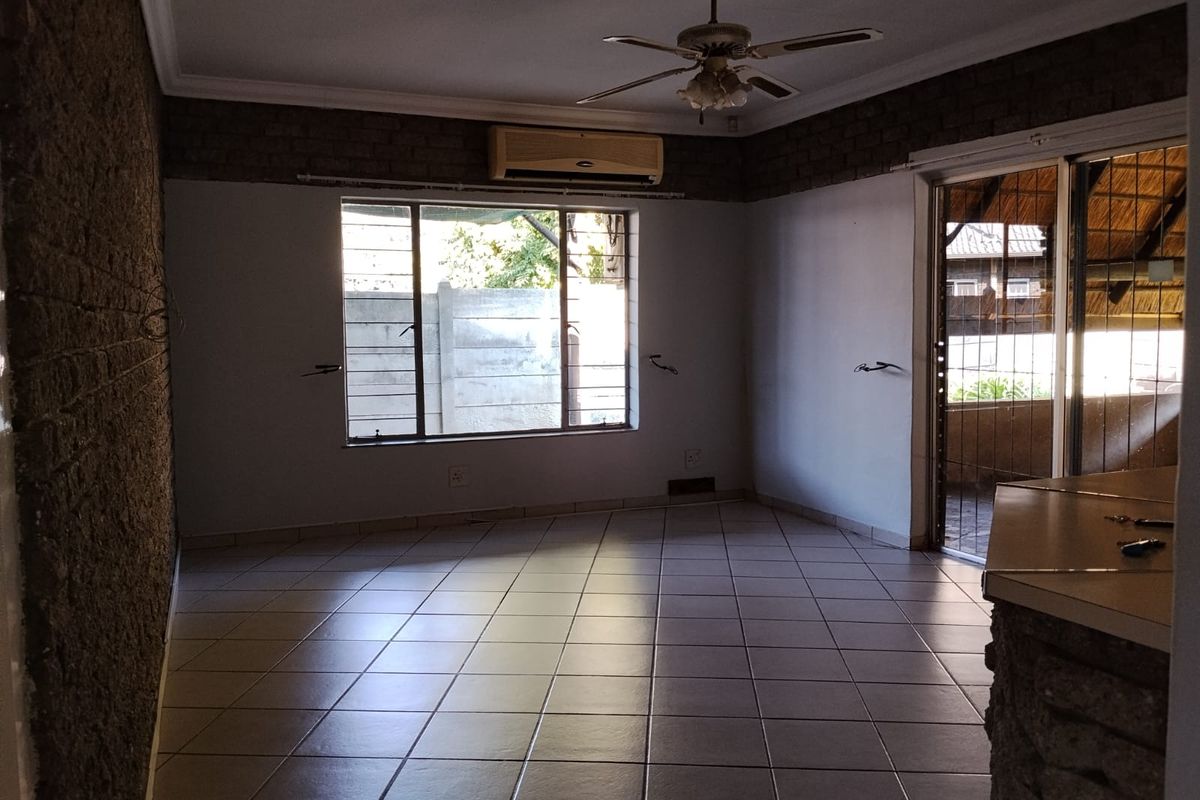 An empty living room featuring tiled flooring, exposed brick accents, a ceiling fan, and a split-system air conditioner with access to an outdoor area.