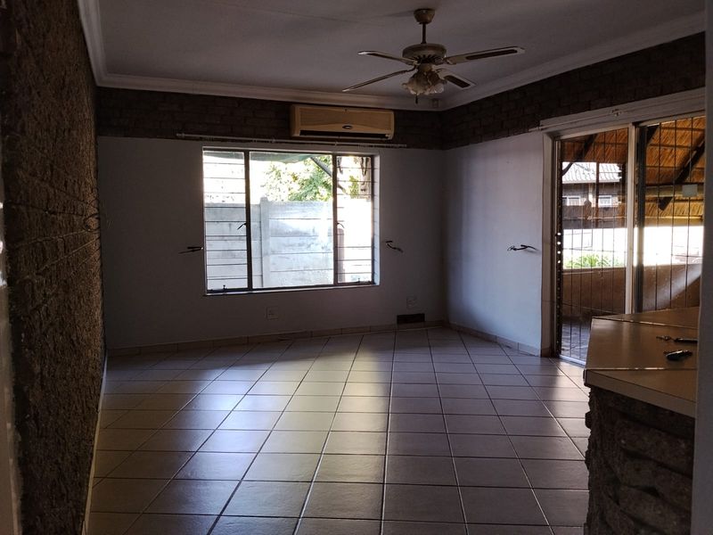 An empty living room featuring tiled flooring, exposed brick accents, a ceiling fan, and a split-system air conditioner with access to an outdoor area.