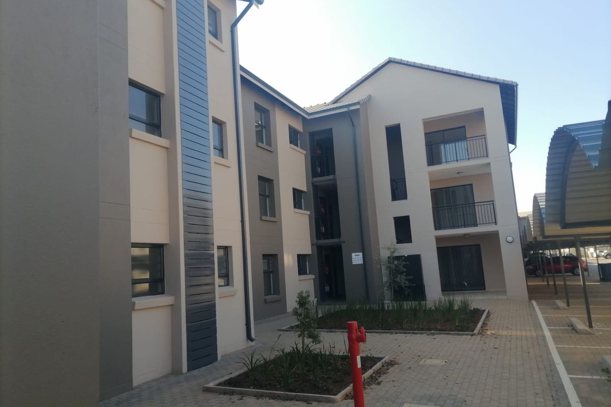 Exterior view of a modern apartment complex featuring paved walkways, landscaped garden beds, and covered parking bays.
