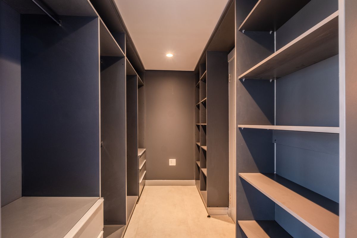 A modern walk-in closet featuring dark built-in cabinetry with extensive shelving and hanging space, finished with neutral tiled flooring and recessed lighting.