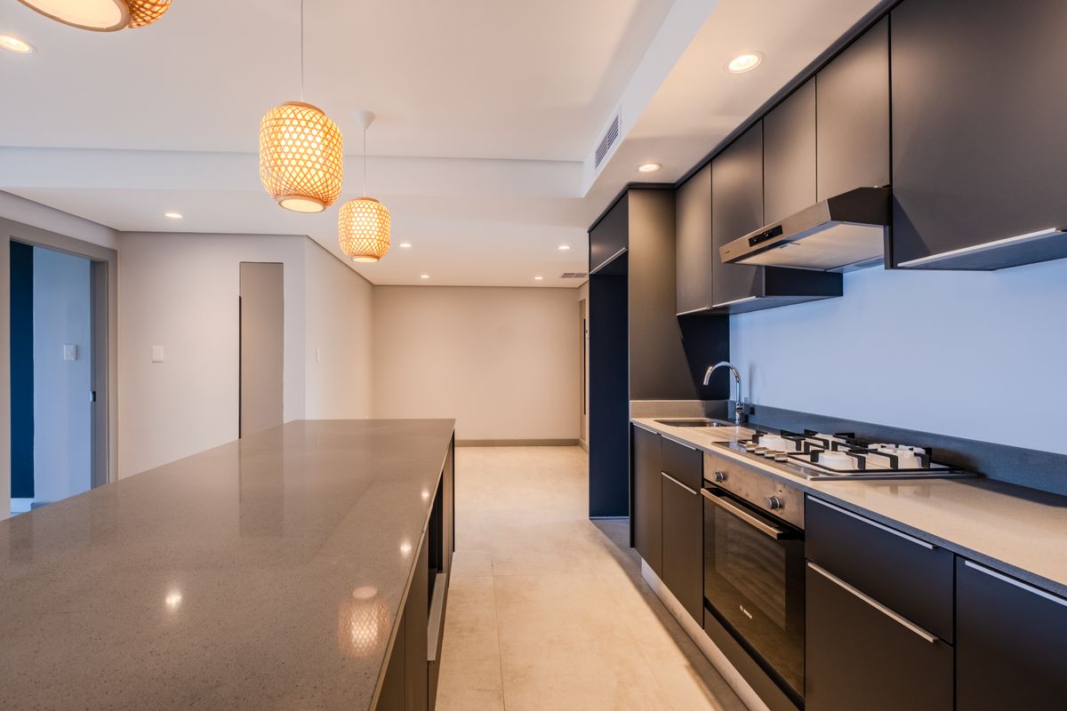 Modern kitchen featuring sleek dark cabinetry, stone countertops, integrated gas hob, oven, and extractor fan, complemented by recessed lighting and a spacious island.
