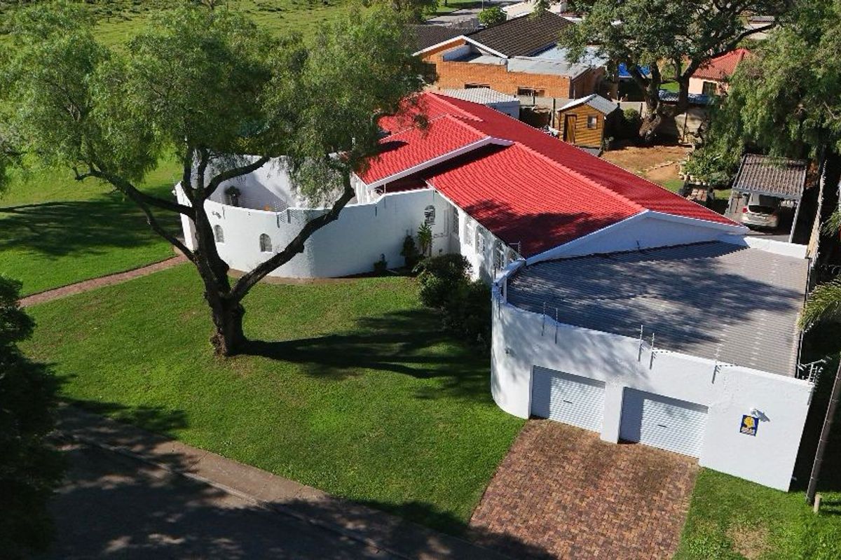 Aerial view of a residential property featuring a distinctive white facade, red metal roof, and a double garage with a paved driveway.