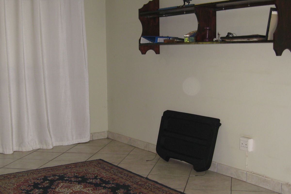 A simple living area featuring tiled flooring, neutral wall paint, and a wall-mounted wooden shelf unit.