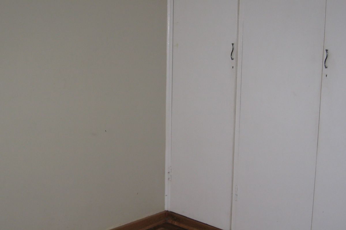 A corner view of a bedroom featuring built-in cupboards with white doors and parquet flooring.