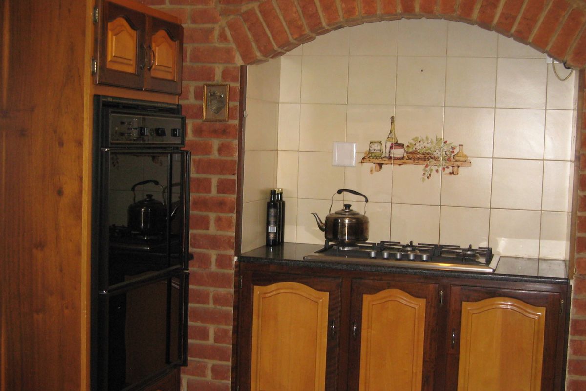 A traditional kitchen featuring a built-in oven, gas cooktop, and decorative brick archway with tiled splashback.