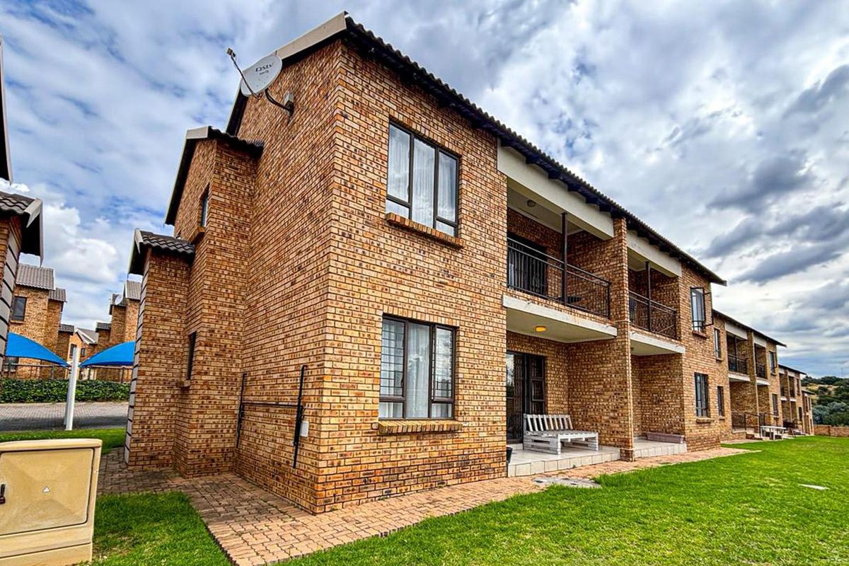Rear view of a multi-story townhouse complex featuring face brick construction, private balconies, paved patio areas, and a shared lawn.